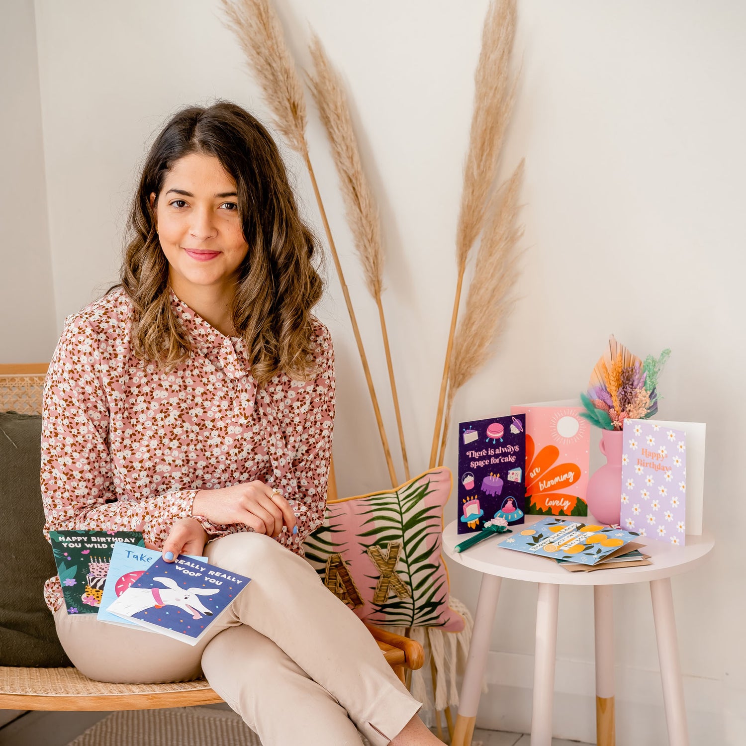 Founder of Gabi & Gaby, Gabi Maksimov sitting in a chair holding a selection of greeting cards